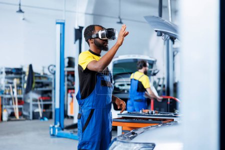 Photo for African american engineer in auto repair shop using virtual reality to visualize car battery in order to fix it. Skilled garage worker wearing futuristic vr headset while working on broken vehicle - Royalty Free Image