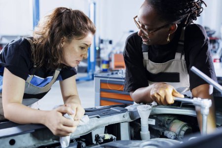 Photo for Skilled engineers in auto repair shop working together on fixing car, discussing best options. Teamworking employees collaborating on servicing broken vehicle, checking for damaged steering mechanism - Royalty Free Image