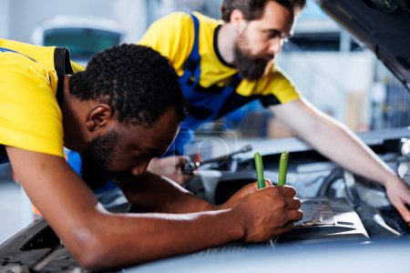 Photo for Repairman and coworker collaborating on servicing broken vehicle, checking for faulty engine. Certified mechanics in auto repair shop working together on fixing car, discussing best options - Royalty Free Image