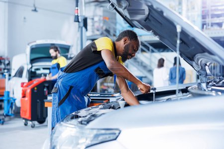 African american mechanic in car service uses torque wrench to tighten nuts after replacing broken engine. Proactive garage employee uses professional tools to fix client automobile