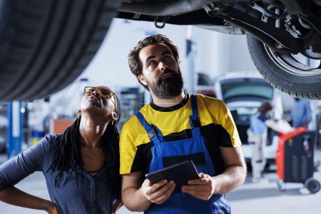Hardworking specialist helping customer with car checkup in auto repair shop. Skilled garage worker looking over automobile parts with woman, repairing her broken vehicle wheels during inspection