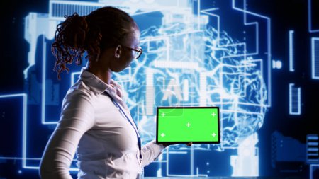 Technisch versierter Administrator im Rechenzentrum mit Tablet-Attrappe, die künstliche Intelligenz nutzt, um Denkprozesse im menschlichen Gehirn zu simulieren. Afroamerikanerin arbeitet mit neuronalen Netzwerkalgorithmen der KI