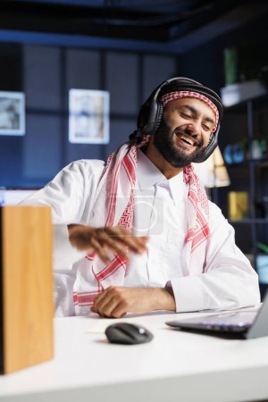 Musulman gars utilisant la technologie sans fil pour la communication en ligne et la recherche. Avec un ordinateur portable et un casque sans fil, il s'engage avec enthousiasme dans la vidéoconférence et écoute attentivement.