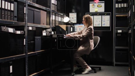 Photo for Leaving the office filled with documents and clues is caucasian woman with experience in criminal investigations. Female detective exits workstation with laptop bag after gathering clues and evidence. - Royalty Free Image