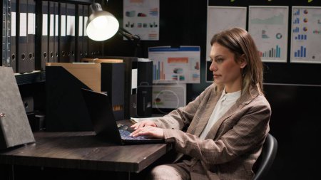 Confident female private detective investigator reviews clues in office, searching on laptop for evidence to solve crime. Profile portrait of focused caucasian policewoman using personal computer.