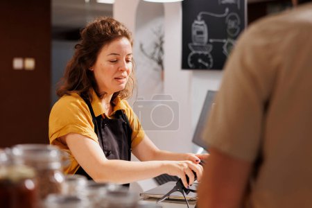 Photo for Vendor at zero waste supermarket checkout counter using bar code scanner to process customer order. Seller in eco friendly local neighborhood shop scanning client groceries - Royalty Free Image