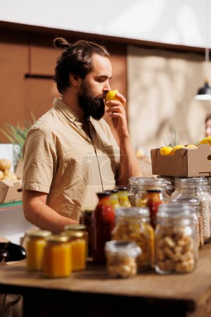 El hombre en la tienda de residuos cero huele limones, asegurándose de que sean recogidos a mano y cultivados en la granja. El cliente vivo verde que comprueba minuciosamente los artículos alimenticios del supermercado local es libre de productos químicos