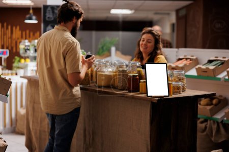 Tableta Mockup con espacio de copia vacío utilizado como signo publicitario en el supermercado de cero residuos lleno de clientes que compran alimentos saludables. Dispositivo de pantalla aislada en la tienda de barrio local