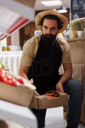 Trader adding crates full of farm grown vegetables from his own garden on zero waste shop shelves. Storekeeper restocking local neighborhood store with chemicals free food items