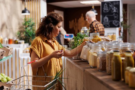 Grüne lebende Frau in Zero-Waste-Laden interessiert sich für den Kauf von Massenprodukten mit hohem Nährwert. Kunde kauft Speisekammer-Heftklammern in nachhaltigem Supermarkt vor Ort