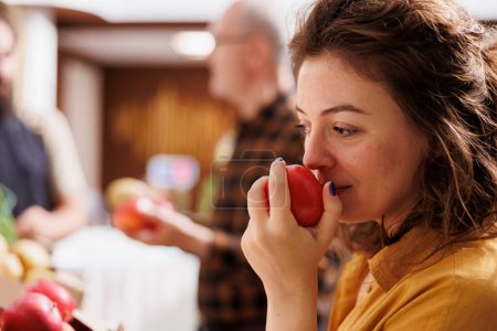 Photo for Woman smelling organic handpicked apples in zero waste supermarket while vendor talks with elderly customer in blurry background. Client testing to see if local neighborhood shop fruits are fresh - Royalty Free Image