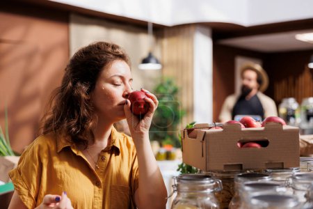 Frau genießt den Geruch von Äpfeln aus biologischem Anbau im umweltfreundlichen Zero Waste Store. Kundentest, um zu sehen, ob die Früchte des lokalen Nachbarschaftsladens frisch sind und keine Zusatzstoffe enthalten