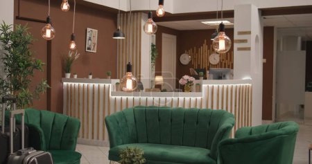 Empty hotel entrance lounge area with luxurious sofa and modern indoors furniture, fashionable hotel retreat. Classy decorations with stylish lights and plants at reception front desk.
