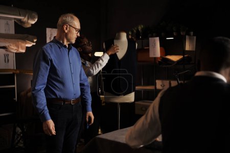 Photo for African american tailor showing vest on mannequin to elderly customer looking to buy stylish premium quality suit for business meeting. Professional suitmaker crafting bespoke garment for client - Royalty Free Image