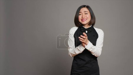 Photo for Asian server applauding someone and cheering for success, saying congratulations in front of camera. Waitress in formal uniform clapping hands, doing standing ovation gesture. Camera A. - Royalty Free Image