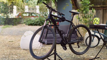 Dans la cour, vélo placé sur le stand de réparation prêt pour un examen minutieux et la correction des composants cassés. Entretien extérieur de vélo d'été avec équipement professionnel.