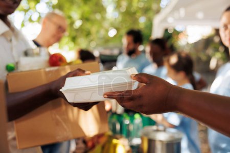 Photo for Volunteer of african american descent offers warm meal to an impoverished and hungry individual. Photo focus on the less fortunate person receiving complimentary food from charitable worker. - Royalty Free Image