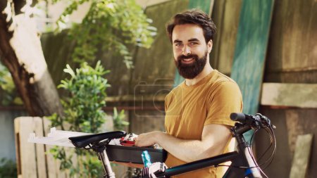 Photo for Portrait shot of sports enthusiast man carrying and checking toolbox ready for annual bike maintenance in yard. Enthusiastic male cyclist grasping specialized toolkit to fix broken bike outdoor. - Royalty Free Image