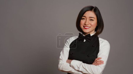 Die Gastgeberin posiert selbstbewusst im Studio, die Arme über dem grauen Hintergrund verschränkt. Asiatische Kellnerin Barista mit Gourmet-Know-how serviert lächelnd in die Kamera. Kamera B.