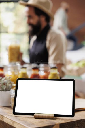 Close-up of digital tablet with a white screen display is horizontally placed on a wooden counter. Selective focus on smart device displaying isolated copyspace mockup template.