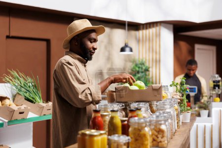 An African American guy picking fresh fruits and veggies and admires organic, sustainable products. The market promotes local farmers by providing healthful foods with a reduced carbon footprint.