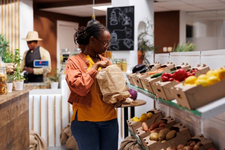African American woman explores a modern eco friendly grocery store, browsing a variety of fresh, organic products with sustainable packaging. The storekeeper provides excellent customer service.