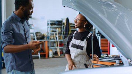 Photo for Experienced repairman assisting customer with car maintenance in repair shop. Certified worker in garage looking over car components with man, servicing his vehicle during routine checkup - Royalty Free Image