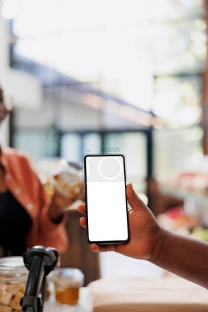 Photo for Detailed view of cell phone grasped by african american person, displaying isolated white screen for sustainable bio food store commercials. Closeup of mobile device showing blank mockup template. - Royalty Free Image