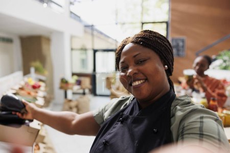 Black woman running a zero-waste shop uses selfie camera on her phone to promote environmentally responsible vegan products online. Female store owner of bio supermarket creates marketing content.