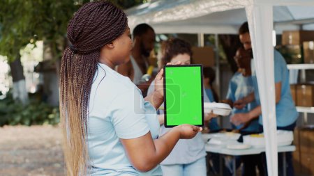 Una plantilla de cromakey aislado para los mensajes humanitarios en la tableta inteligente es llevado a cabo por el trabajador de caridad afroamericano. Mujer negra voluntaria agarrando dispositivo digital con pantalla verde en blanco.