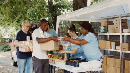 Bedürftige Personen werden von engagierten Freiwilligen mit Essensboxen und Konserven versorgt. Lächelnde Mitarbeiter der Hilfsorganisation Food Drive und Non-Profit-Organisation ernähren die Obdachlosen.