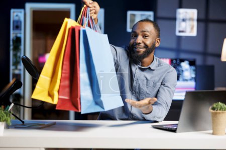 Afroamerikanischer Mann filmt Mode-Vlog, hält Einkaufstüten in der Hand und zeigt Abonnenten Einkäufe, die er vor kurzem bekommen hat. Internet-Show-Moderator präsentiert Zuschauern Neuerwerbungen und filmt sich selbst zu Hause