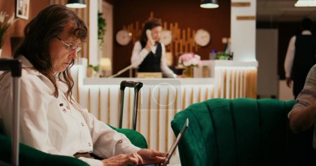 Couple de personnes âgées passant du temps dans le salon, femme utilisant un ordinateur portable pour créer un itinéraire de vacances tandis que l'homme aime la conférence sur le canapé. Personnes à la retraite attendant de voir un hébergement à l'hôtel.