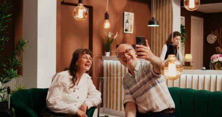 Ältere Paare unterhalten sich auf Online-Videokonferenz mit Neffen auf Auslandsreisen, Internet-Videokonferenz-Verbindung, um Urlaubspläne zu präsentieren. Menschen vertreiben sich die Zeit im Lounge-Bereich des Hotels.