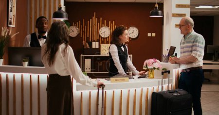 Elderly people arriving in hotel lobby to see accommodation, travelling on retirement holiday with all inclusive room services. Husband and wife talking to concierge about senior travel offers.