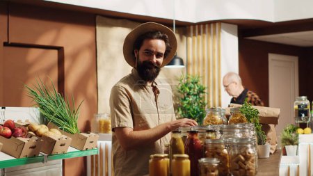Porträt eines glücklichen veganen Mannes im Zero-Waste-Supermarkt mit Einkaufskorb, um Massenware in ökologischen Containern zu kaufen. Klient im lokalen Nachbarschaftsladen kauft konservierungsstofffreie Lebensmittel