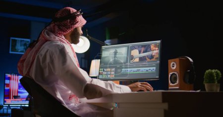 Photo for Arabic colorist freelancer wearing headphones while editing project, stitching videos together, working with images and sounds. Self employed man processing movie on PC workstation - Royalty Free Image