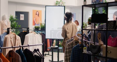 Photo for Customer in shopping outlet using AR tech kiosk to look at cheap and sustainable clothes. Client in eco friendly second hand store using led screen to choose between garments - Royalty Free Image
