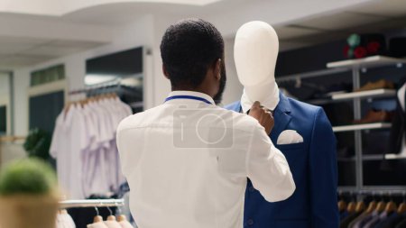 Empleado apretando elegante blazer corbata en maniquí en tienda de ropa de lujo. Trabajador que arregla la nueva colección de prendas de vestir elegantes de alta clase en la boutique de moda premium