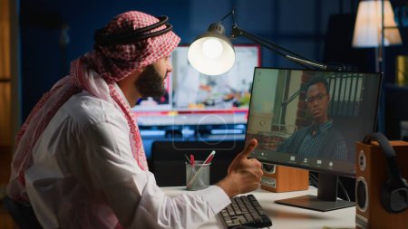 Téléchargez les photos : Télétravailleur arabe en séance d'appel vidéo avec le thérapeute, demander des conseils, se sentir déprimé. Employé musulman travaillant à distance en consultation en ligne avec un psychologue de la maison confortable élégant - en image libre de droit