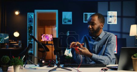 BIPOC online star filming tech review of newly released wired gaming mouse, keyboard and headphones, giving viewership feedback and presenting specifications, handheld camera