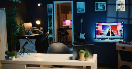 Interior del acogedor estudio en casa vacío con dispositivos de grabación profesionales utilizados para la producción de programas de Internet. Apartamento lleno de equipamiento técnico, TV en segundo plano y animaciones en pantallas de ordenador