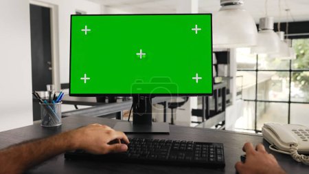 Photo for POV of businessman works at greenscreen pc in front of computer, solving daily tasks and looking at monitor running blank chromakey template at workstation. Worker uses mockup screen. Tripod shot. - Royalty Free Image