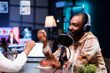 Lächelnder schwarzer Mann beim Faustschlag mit einem afrikanisch-amerikanischen Moderator vor Beginn der Live-Radiosendung. Fröhlicher männlicher Influencer begrüßt Gast bei Aufzeichnung von Online-Talkshow.