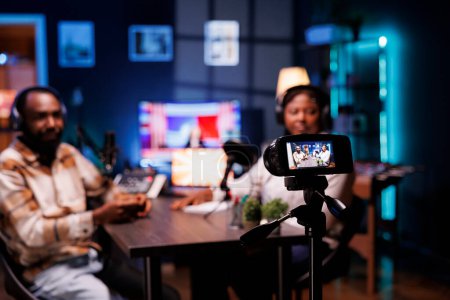 Photo for During live broadcast, podcast host records guest sharing engaging story with audience by mounting professional device on a tripod. Camera taking video of bloggers delivering facts in home studio. - Royalty Free Image