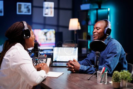 Female interviewer having live discussion with black man, recording a radio show. African american couple using audio equipment in home studio, talking and making a podcast episode.