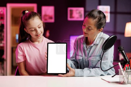 Daughter and parent filming content about best mockup tablets on the market in neon pink lit apartment. Young media star and mother recording isolated screen device review