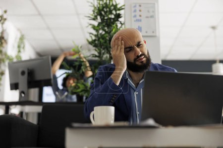 Démarrer exécutif souffrant de migraine tout en faisant la gestion de projet sur ordinateur portable dans le bureau d'affaires. Entrepreneur épuisé ayant mal à la tête tout en travaillant à la recherche marketing numérique