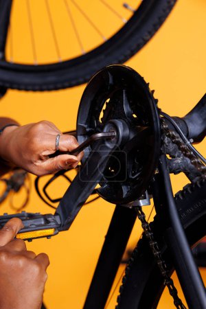 Photo focus on pair of hands using multitool for adjusting and fixing damaged bicycle parts. Detailed image of african american person holding expert work tool for fixing the crank arm of broken bike.