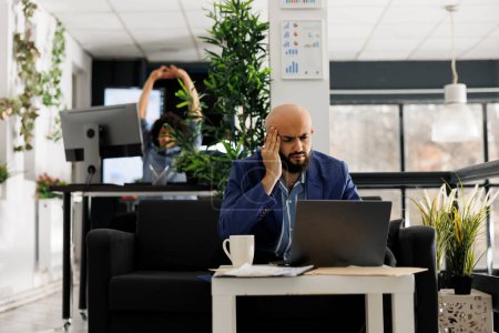 Téléchargez les photos : Gestionnaire exécutif arabe souffrant de migraine tout en travaillant sur ordinateur portable dans le bureau de démarrage d'entreprise. Analyste financier épuisé de l'entreprise ayant mal à la tête et touchant les temples - en image libre de droit